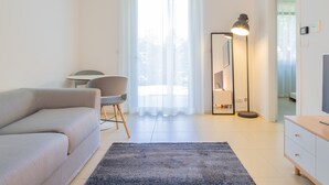 A modern living room with a sofa, a chair, a floor lamp, and a TV. - Modern and with Pool - Apartment Baseventuno 1 (Sirmione)