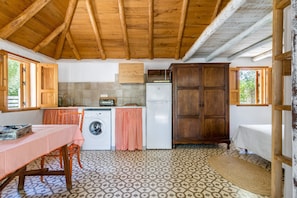 A compact kitchen with a washing machine, wooden cabinets, and a table with a checkered tablecloth. - Studio 'Casita Estudio El Castaño' with Private Pool, Terrace & Wi-Fi (El Palmar, Vejer de la Frontera)
