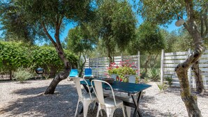 Um pátio externo com mesa e cadeiras, cercado por árvores e um muro.