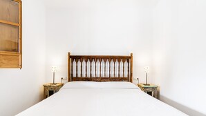 Een groot bed met een houten hoofdbord, twee nachtkastjes met lampen en een effen witte muur.