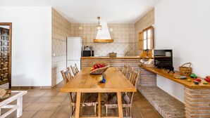 Een eetgedeelte met een houten tafel en stoelen, een keuken met een betegelde spatwand, en een televisie op een aanrecht.