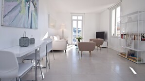 Una sala de estar moderna con un sofá blanco, una mesa de comedor con sillas, un televisor y una estantería.