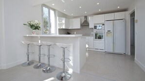 Una cocina moderna con armarios blancos, una isla central con taburetes y electrodomésticos integrados.