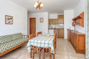Un coin repas avec une table dressée pour quatre personnes, un canapé, des meubles en bois et une cuisine en arrière-plan.