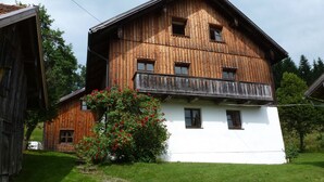 Ein zweistöckiges Holzhaus mit einem Balkon, umgeben von einem Rasen und einem kleinen Garten mit roten Blumen.
