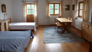 Ein Zimmer mit zwei Betten, einem Esstisch mit Stühlen und großen Fenstern mit Vorhängen.