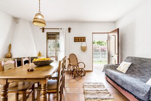 A dining area with a wooden table and chairs, a wicker chair, a hanging basket, and a woven light fixture. - Holiday Home 'El Madroño' with Shared Pool, Private Terrace & Wi-Fi (El Palmar, Vejer de la Frontera)