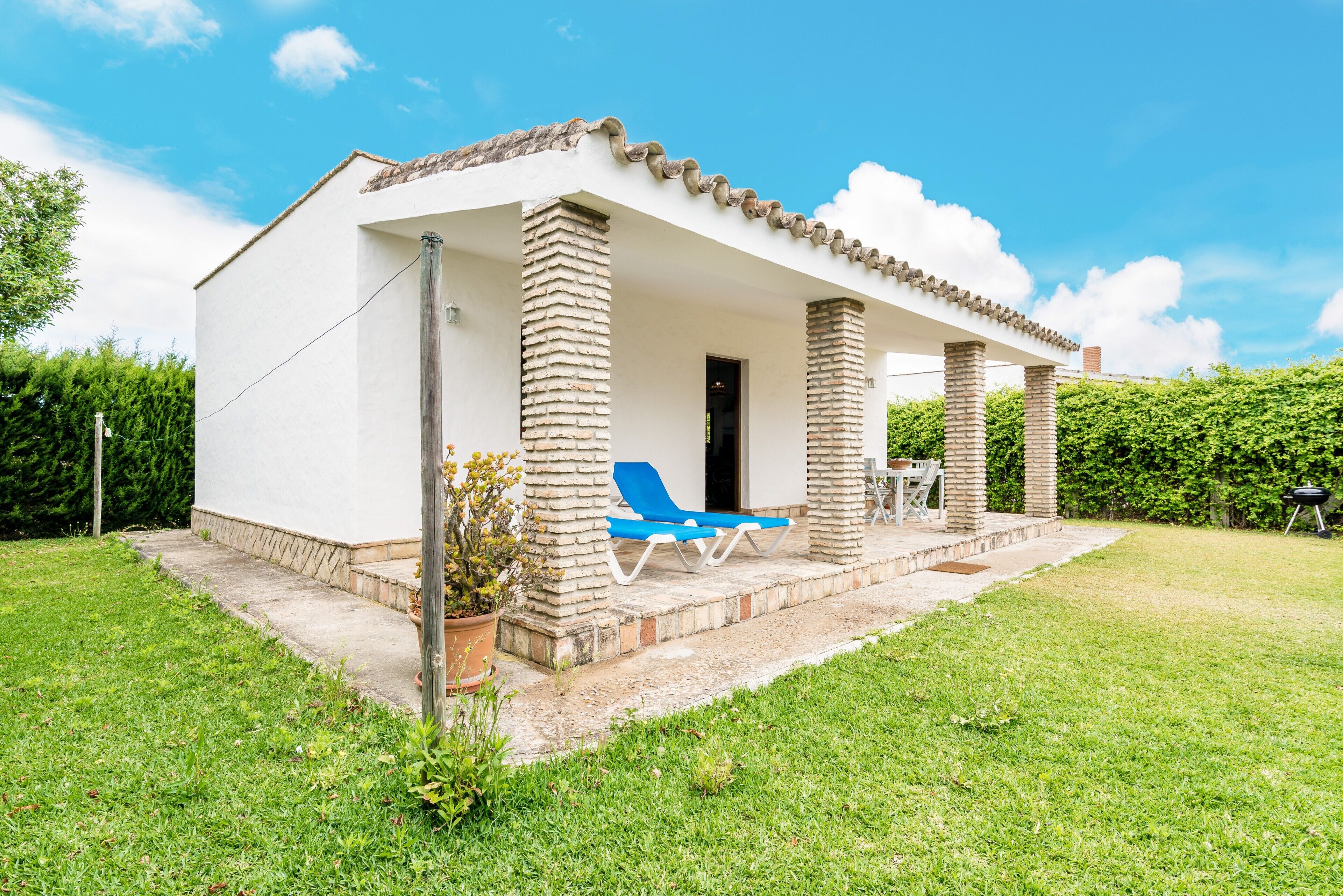 Un bâtiment d’un seul étage doté d’un patio couvert, d’un fauteuil de jardin bleu et d’un barbecue dans la cour.