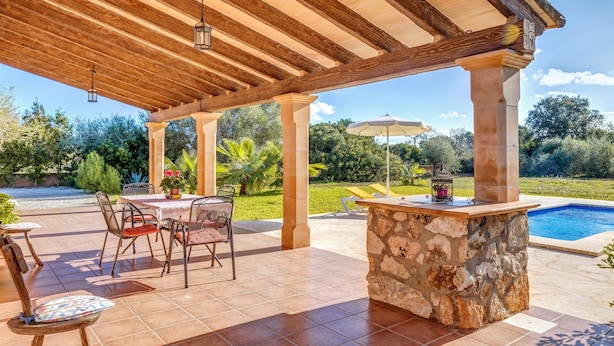 A covered patio with a stone bar, outdoor seating, and a swimming pool.