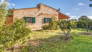 A rustic house with a satellite dish, green shutters, and a small garden.