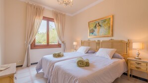 A bedroom with two beds, a painting, a chandelier, and a window with curtains. - Luxurious villa with pool - Villa Torre (cala santanyi)