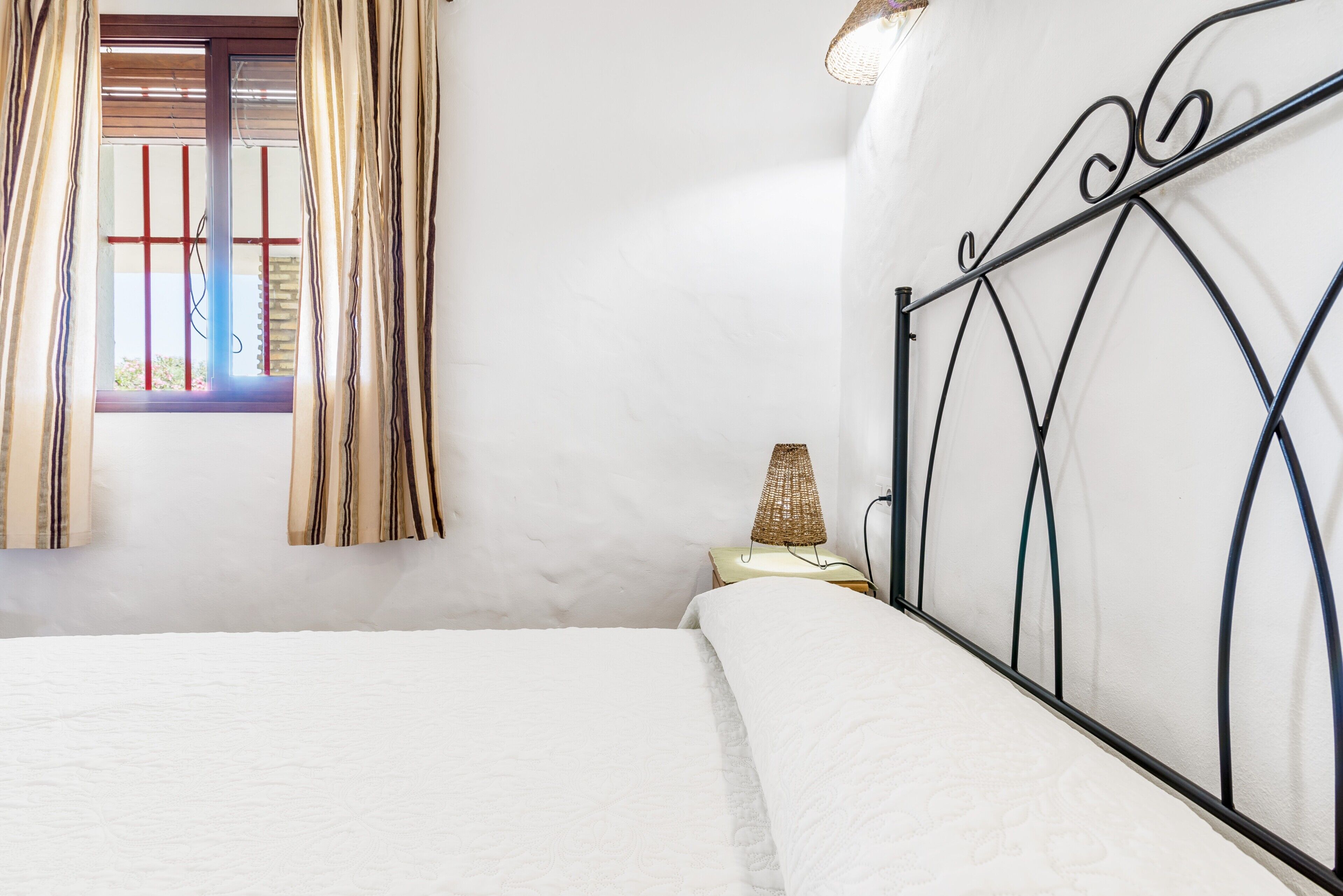 A bedroom with a bed, a nightstand, a lamp, and a window with curtains.