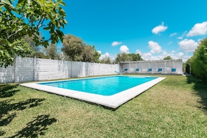 Une piscine rectangulaire entourée d’une clôture blanche, avec une pelouse verdoyante et des arbres en arrière-plan.