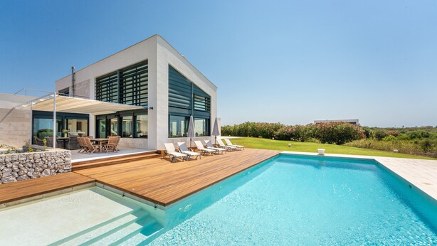 Una casa moderna con piscina, terraza de madera y mobiliario exterior.