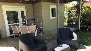 Une terrasse couverte avec deux chaises et une petite table, une porte vitrée et une petite fenêtre.