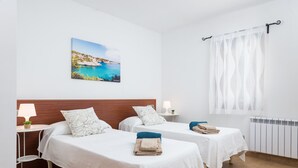 Ein Hotelzimmer mit zwei Betten, Meerblick, einer weißen Wand und einem Fenster mit durchsichtigen Vorhängen.