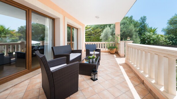 Ein Balkon mit Korbmöbeln, einer Glastür und Blick ins Grüne.