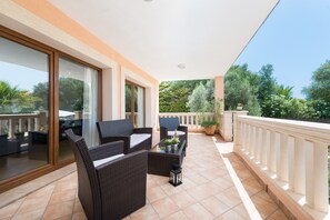 Een balkon met rieten meubels, een glazen deur en uitzicht op groen.