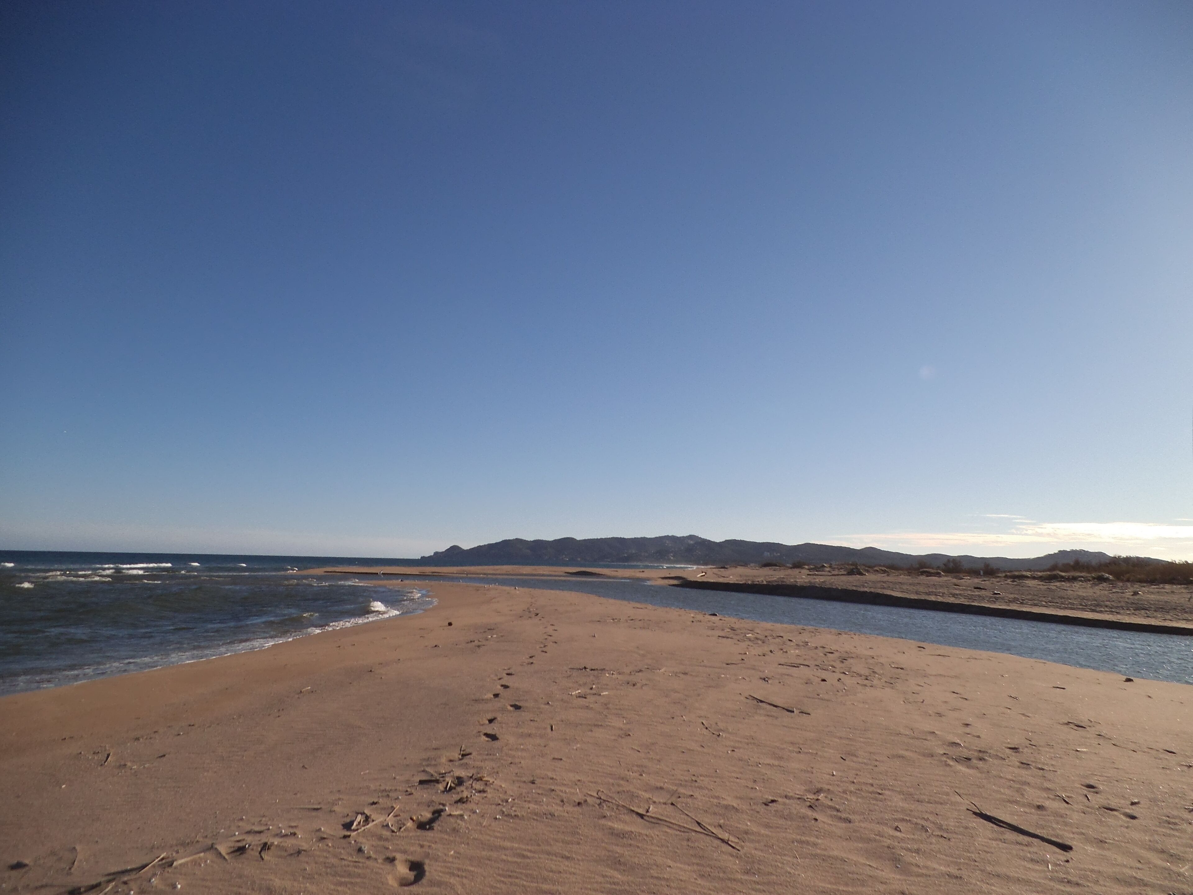 Une vaste plage de sable où l’on peut voir des empreintes de pas qui mènent jusqu’à l’eau.