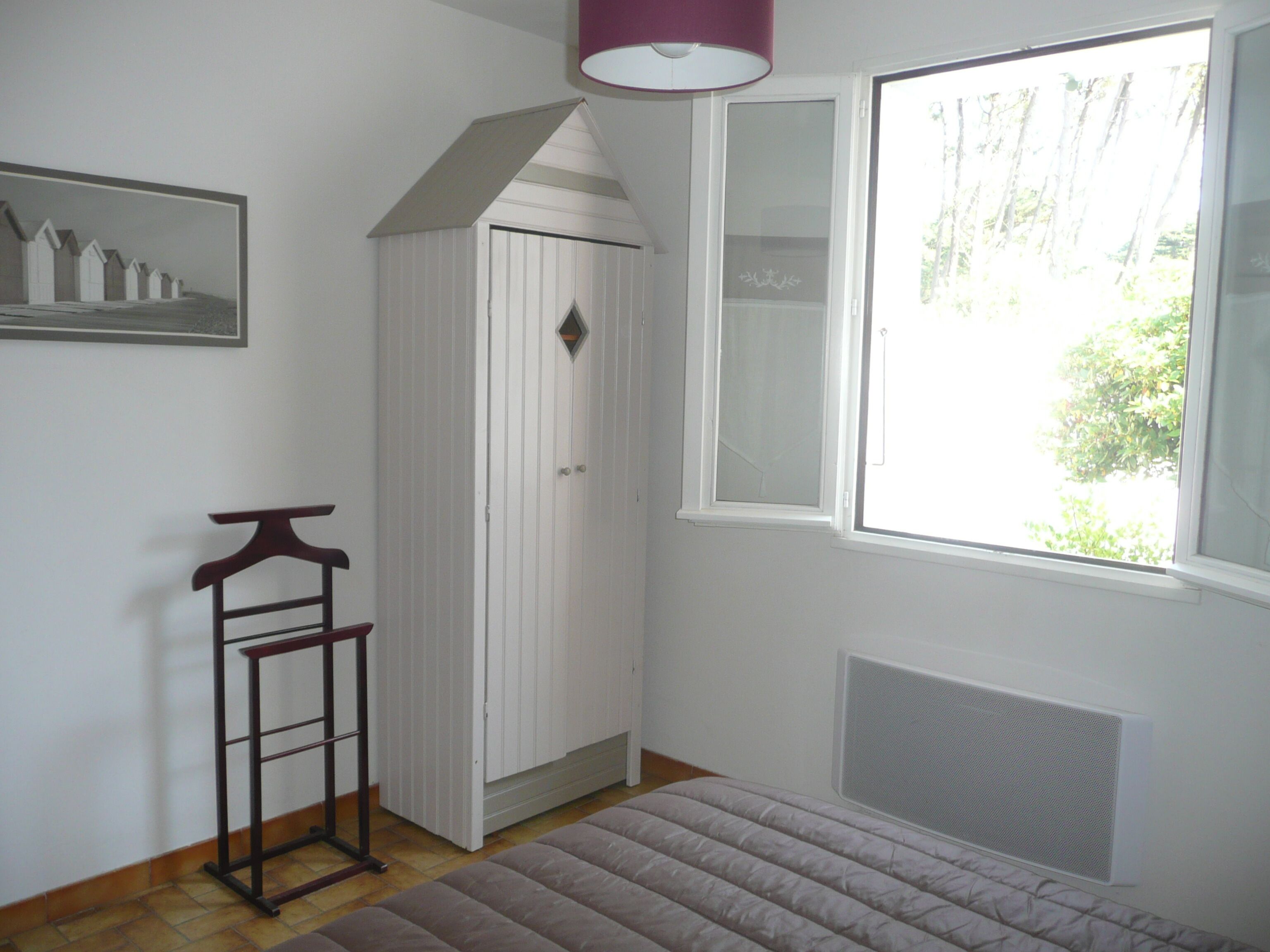 A room with a white wardrobe, a hanging rack, a window with a view of trees, and a radiator.