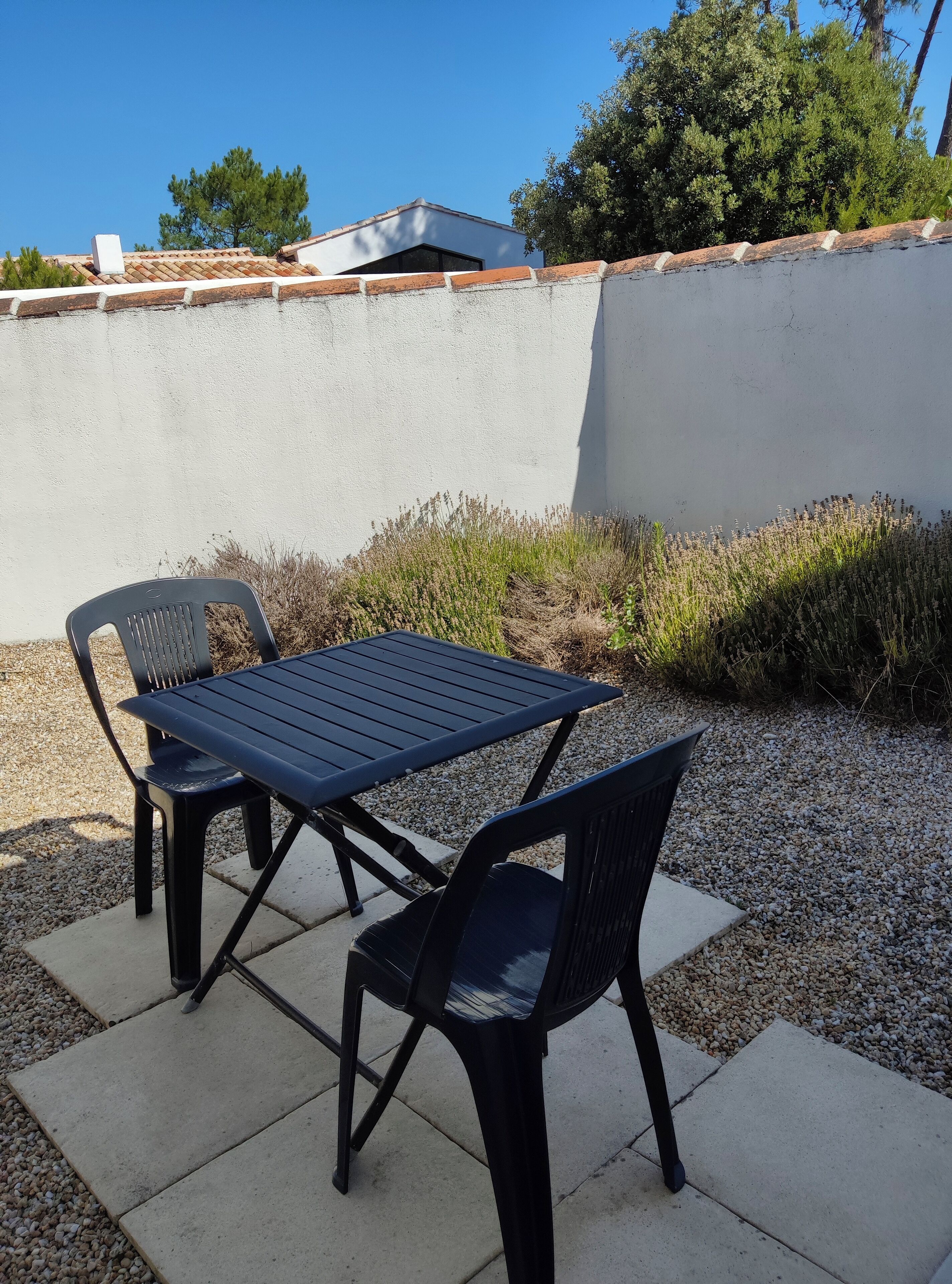 An outdoor patio with a table and two chairs, surrounded by gravel and plants.