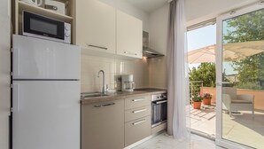 A modern kitchen with a microwave, coffee maker, oven, and sliding glass doors leading to a balcony with potted plants and outdoor furniture. - Villa Green Palm - Apartment 2 (Vrsar)