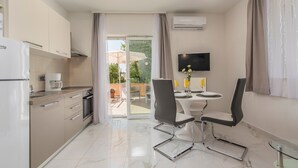 A modern kitchen with a refrigerator, stove, and coffee maker. There is a dining area with a table and chairs, and a TV mounted on the wall. - Villa Green Palm - Apartment 2 (Vrsar)