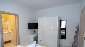 A bedroom with a bed, a wardrobe, a desk with a flat-screen TV, a mirror, and a door leading to a bathroom. - Villa Green Palm - Apartment 2 (Vrsar)