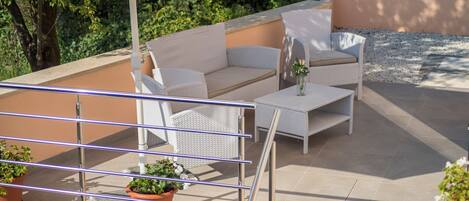 Un patio al aire libre con mobiliario de mimbre, una mesa y plantas en macetas.