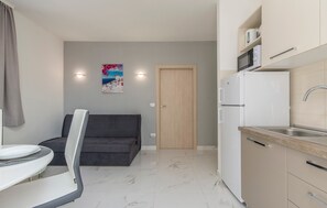 Un espace de vie compact comprenant un coin cuisine, un canapé, une table à manger et une porte donnant sur une autre pièce.