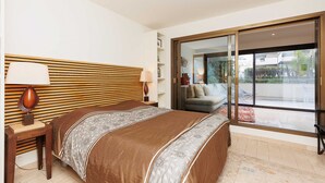 Een slaapkamer met een groot bed, nachtkastje, lamp en een schuifdeur naar een balkon.