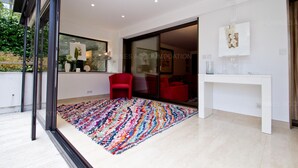 Een modern interieur met een grote glazen deur naar een balkon, een kleurrijk vloerkleed, een rode stoel en een witte console.