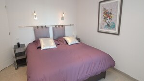 Une chambre à coucher avec un lit, des oreillers, une table de chevet et un luminaire fixé au mur.