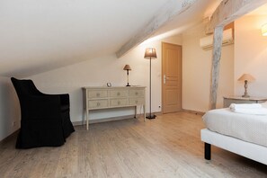 Une chambre avec un plafond en pente, un lit, une commode, deux lampes et une porte.