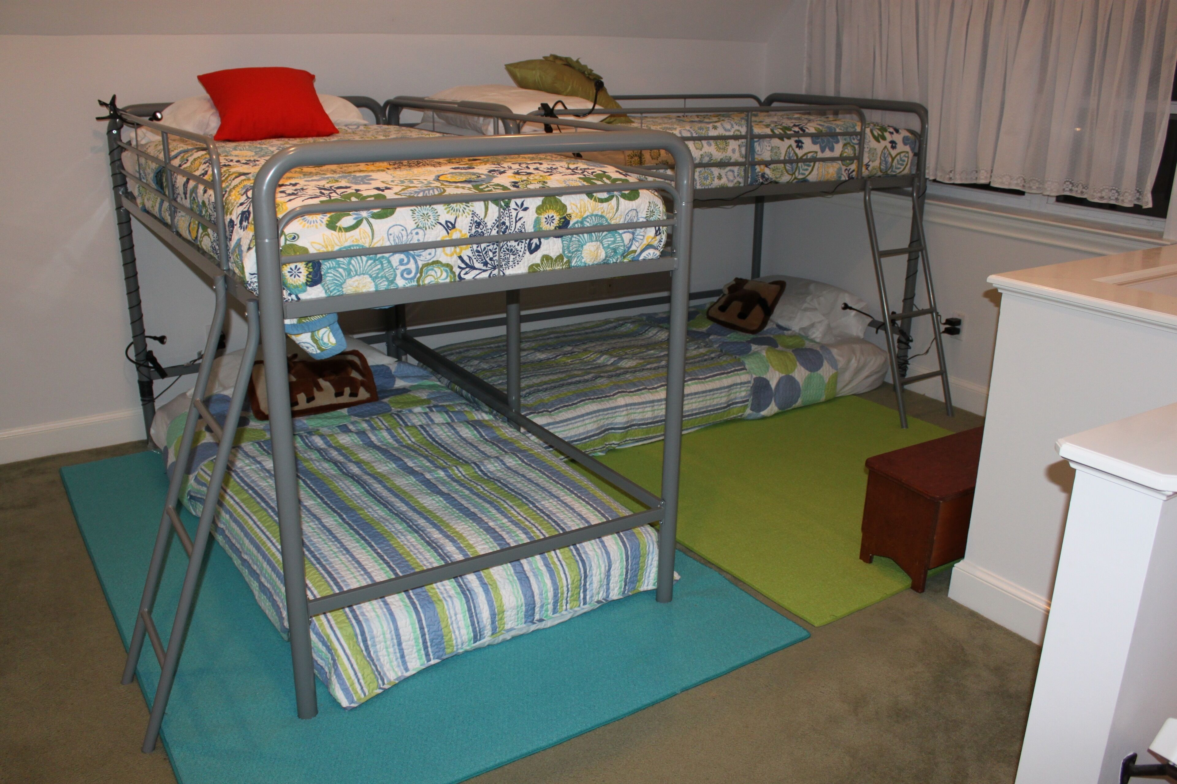 A bunk bed room with two beds, each with patterned bedding and pillows. There is a small wooden stool and a white cabinet.