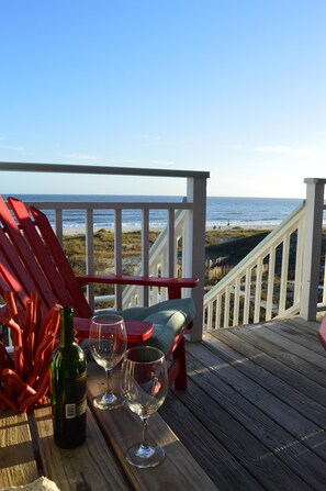 Een houten terras met uitzicht op het strand, een fles wijn en twee lege wijnglazen.