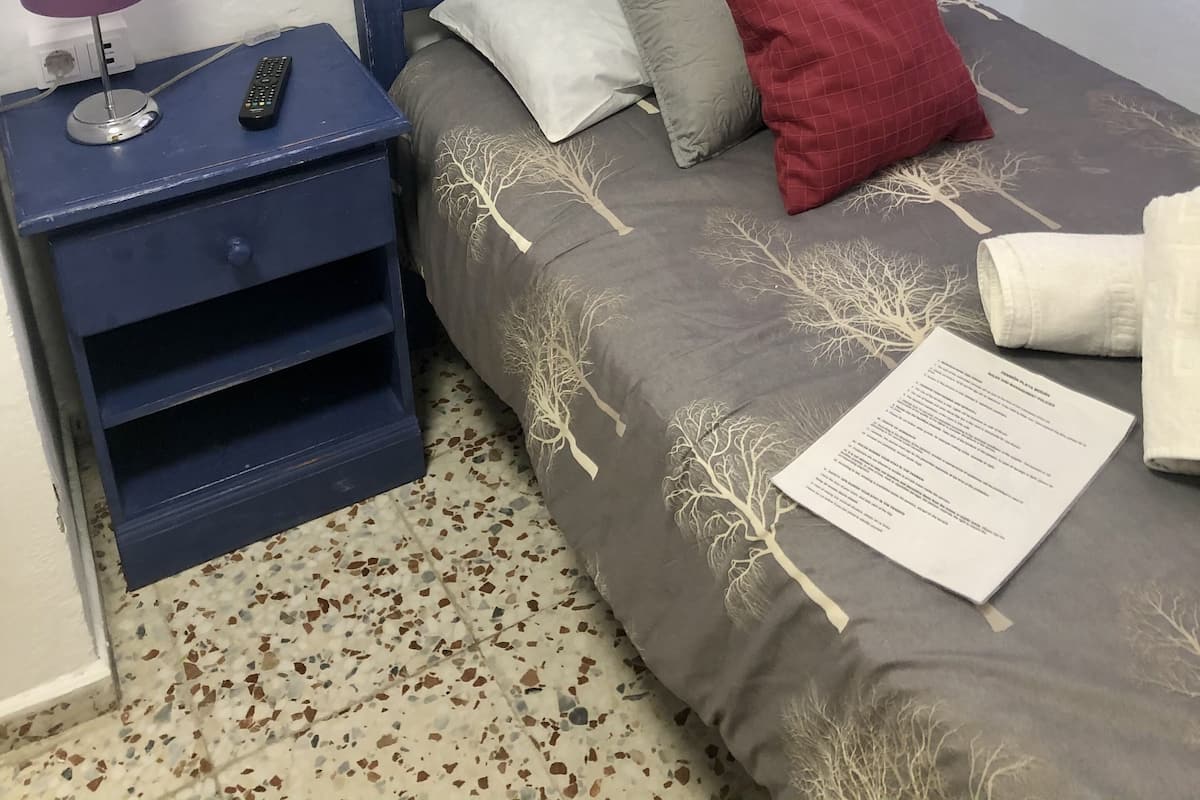 Un dormitorio con una cama, una mesita de noche, una lámpara y un ventanal con cortinas.