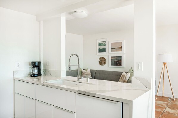 A modern kitchen with a large island, white cabinetry, and a coffee maker. - Mission Beach Paradise with Sweeping Ocean Views - Downstairs Unit 4001 (San Diego)