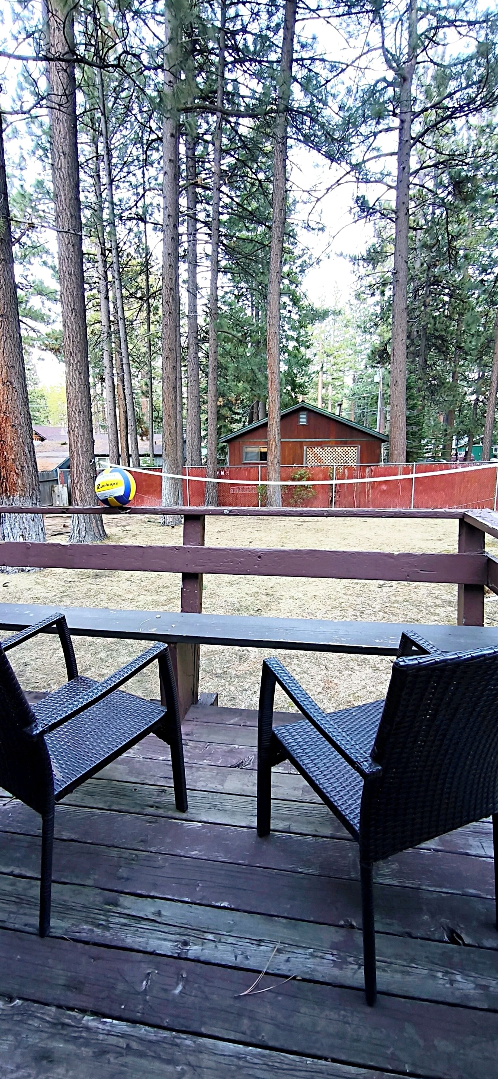 A wooden deck with metal chairs, a volleyball net, and a cabin in the background.