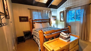 A wooden bed with a checkered bedspread, a bedside table with a stack of folded towels, and a window with curtains. - Tahoe Delight: 5BR, Hot Tub, Sauna, Pool Table & Big Yard ! Close to beach  (South Lake Tahoe)