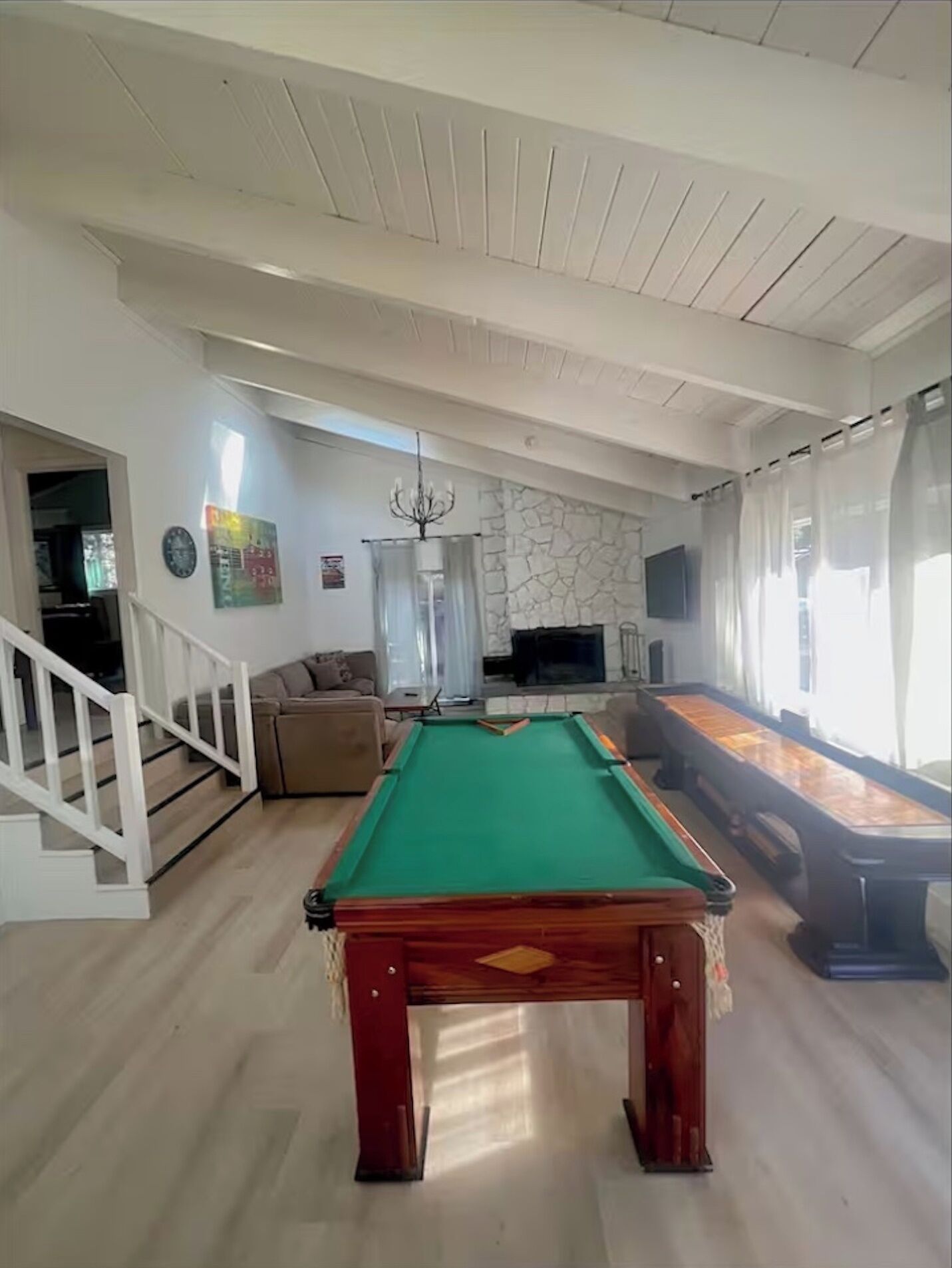 Amplia sala de estar con mesa de billar, chimenea de piedra, televisor y escalera que sube a otro nivel.