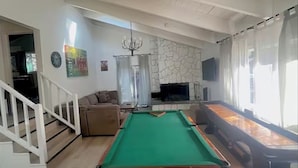 A spacious living room with a pool table, a stone fireplace, a television, and a staircase leading to another level. - Tahoe Delight: 5BR, Hot Tub, Sauna, Pool Table & Big Yard ! Close to beach  (South Lake Tahoe)