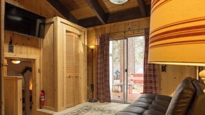 A cozy cabin interior with a wooden interior, a black leather sofa, a fireplace, and a television mounted on the wall. - Tahoe Delight: 5BR, Hot Tub, Sauna, Pool Table & Big Yard ! Close to beach  (South Lake Tahoe)