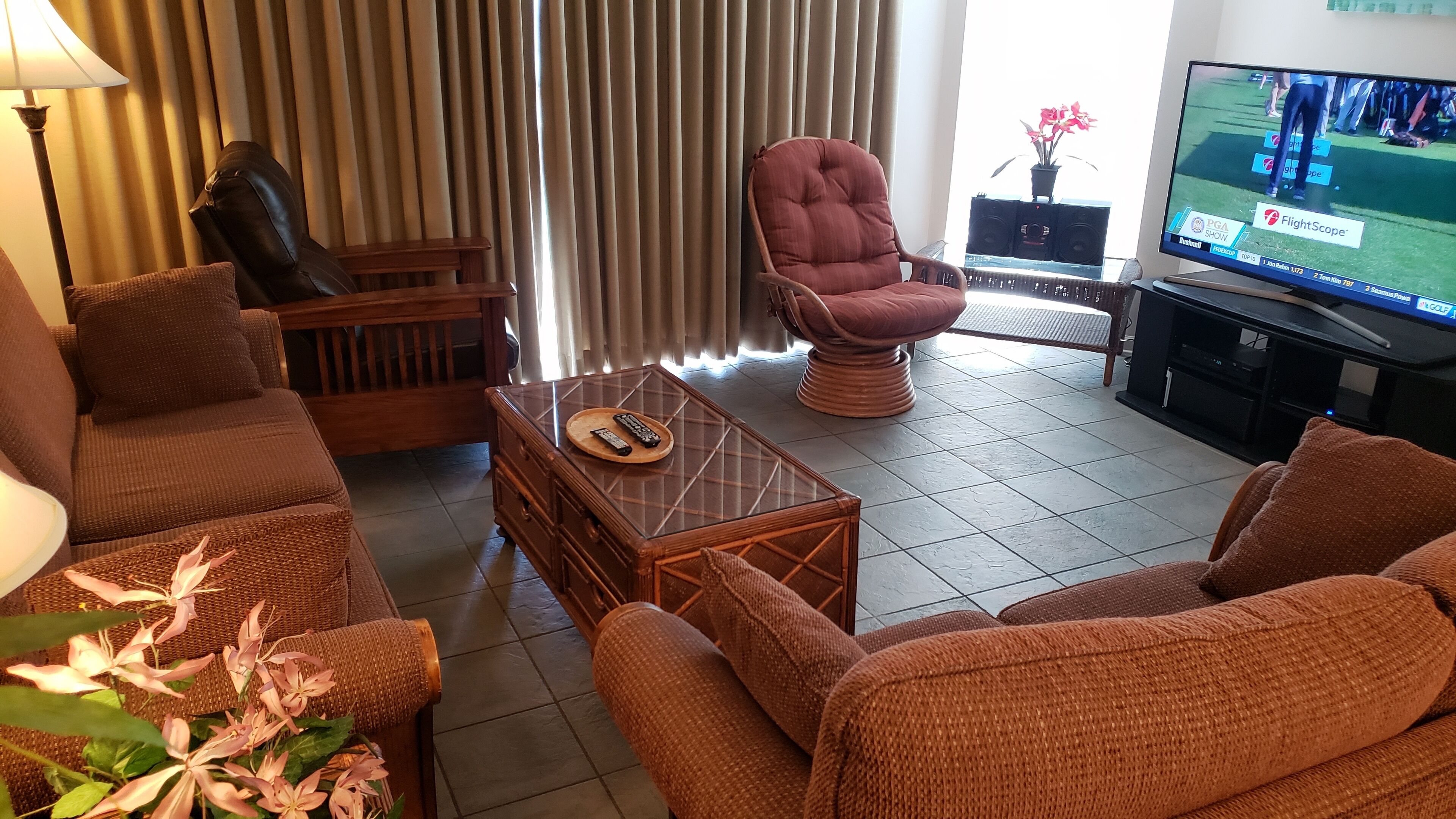A living room with wicker furniture, a glass coffee table, and a television displaying a golf show.