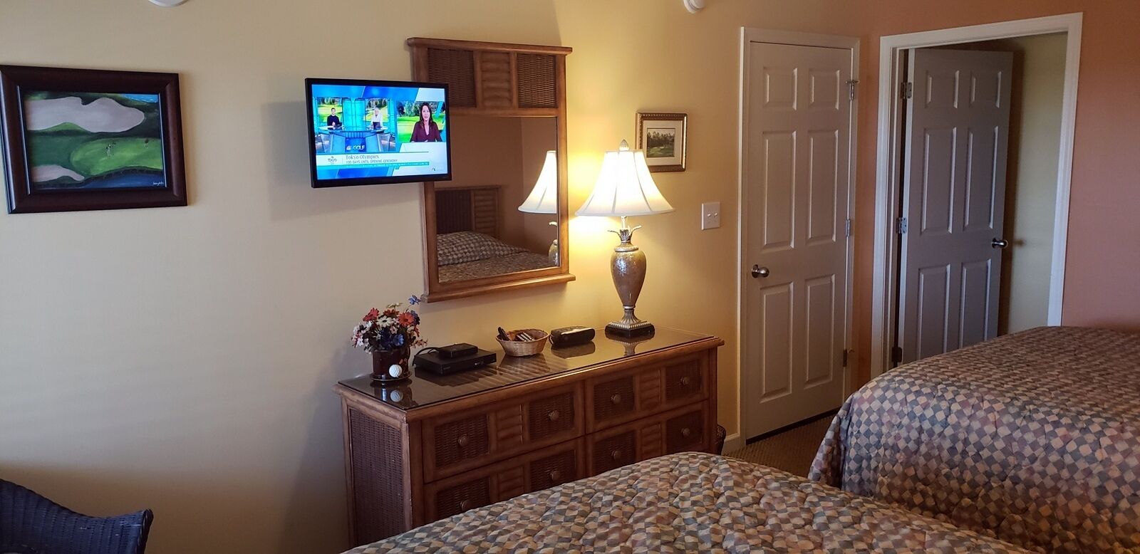 Ein Hotelzimmer mit zwei Betten, einem an der Wand befestigten Fernseher, einem Schminktisch mit Lampe und einer Tür.