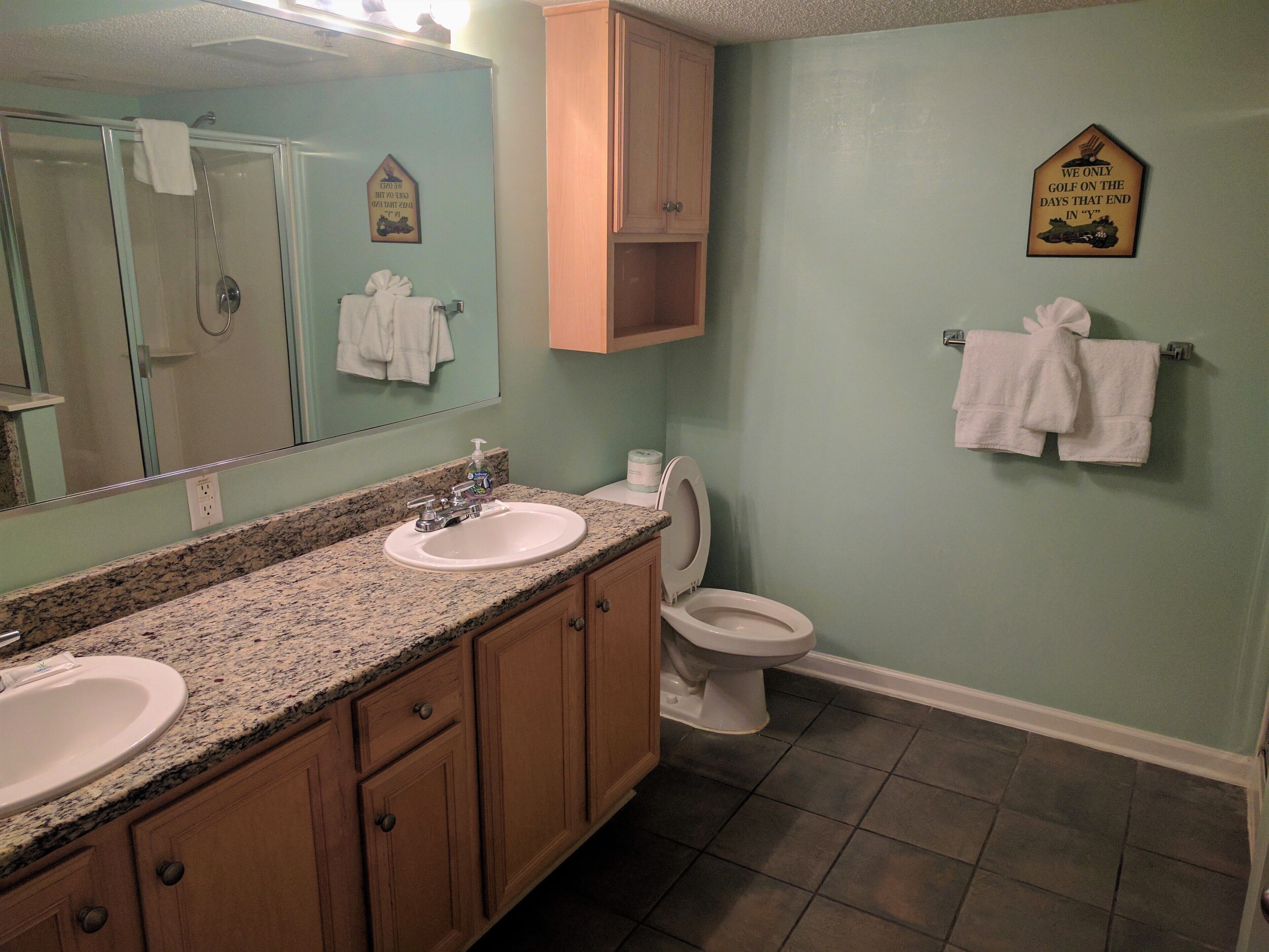 A bathroom with two sinks, a toilet, a shower, and a towel rack.