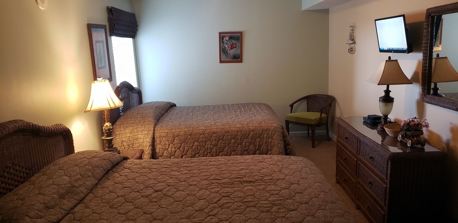 Hotellihuone, jossa on kaksi sänkyä, tuoli, lipasto, televisio ja taulu seinällä.