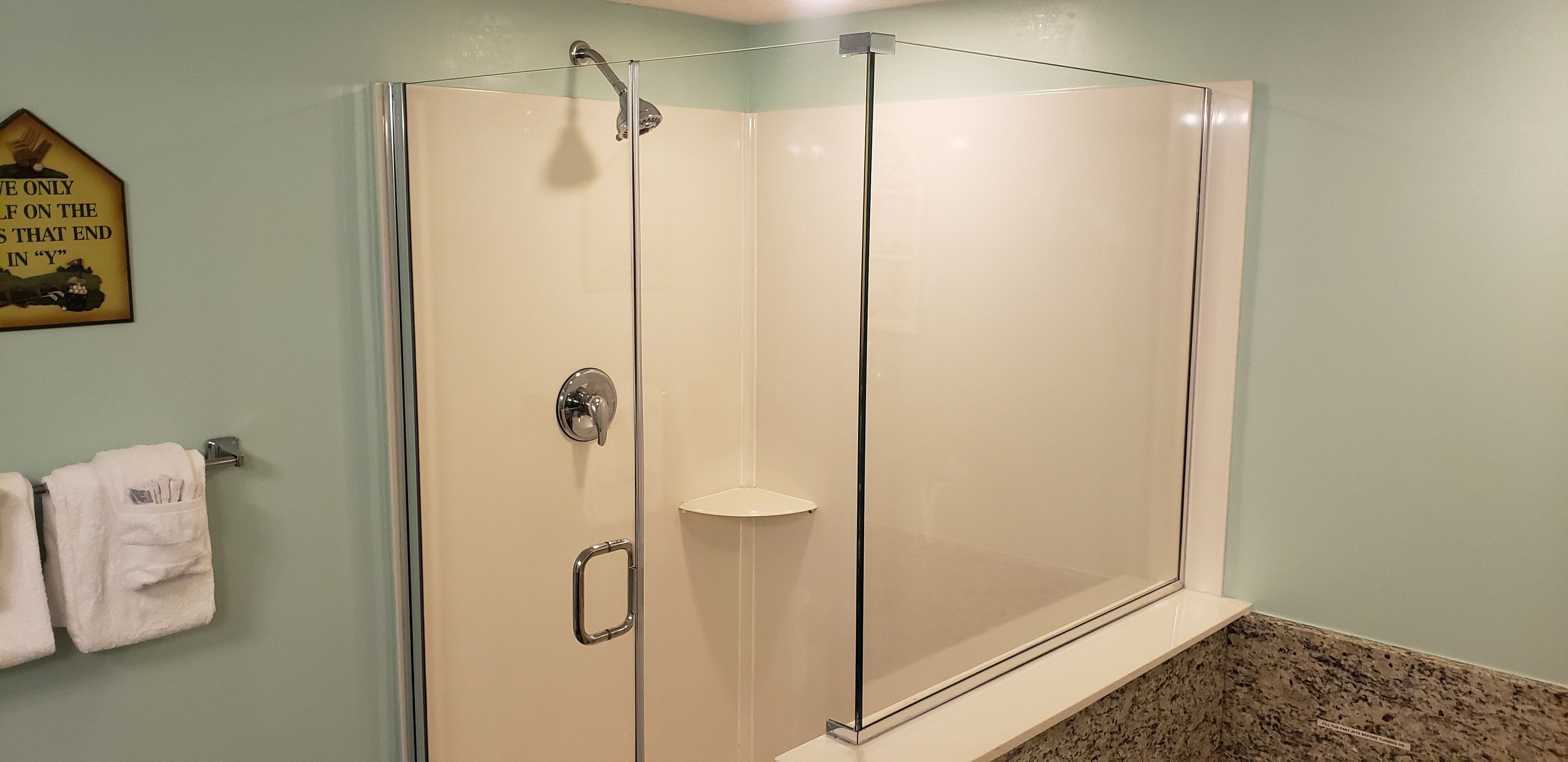 A glass-enclosed shower with a clear door, a towel rack with towels, and a wall-mounted sign.