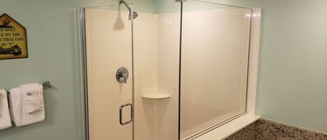 A glass-enclosed shower with a clear door, a towel rack with towels, and a wall-mounted sign.