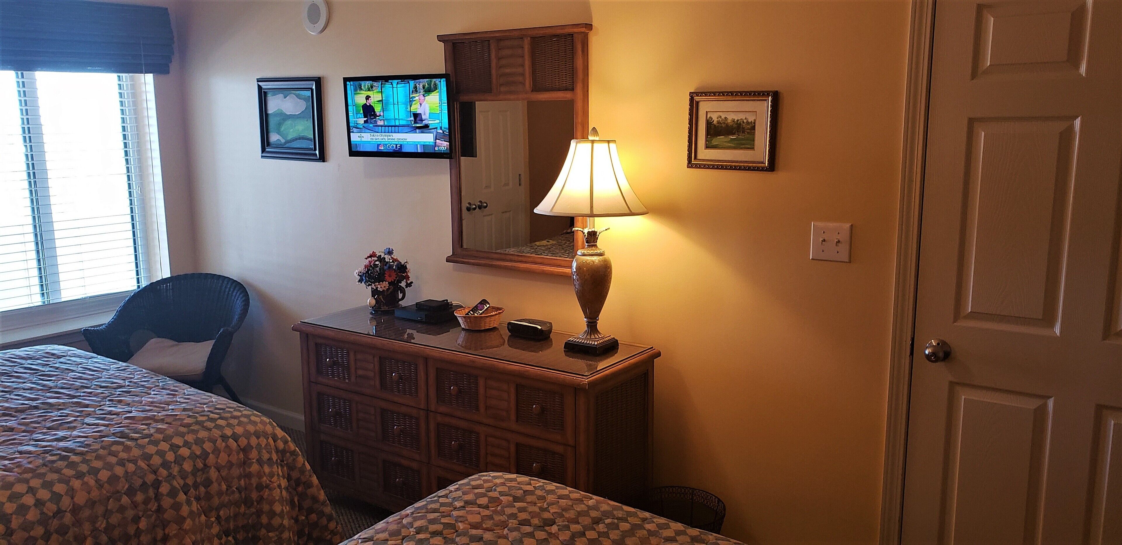 A hotel room with two beds, a dresser, a lamp, a television, and a door.